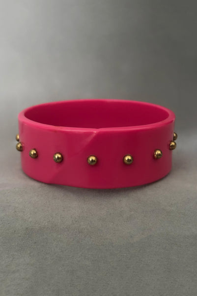 Vertical back view of 1980s vintage pink plastic oval bangle bracelet with gold tone metal studs. Showing a seam on the bangle.