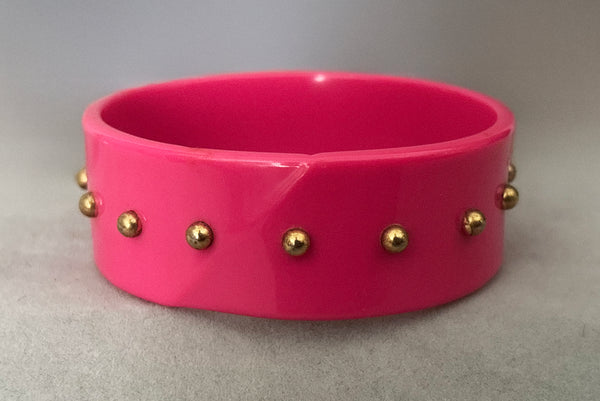 Horizontal back view of 1980s vintage pink plastic oval bangle bracelet with gold tone metal studs. Showing a seam on the bangle.