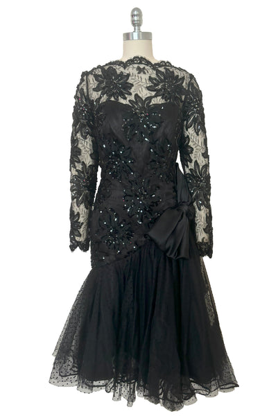 Front view of 1980s vintage black satin, sequin lace, & dotted tulle asymmetrical cocktail dress by Mignon, small to medium. New with tags. Showing the sweetheart strapless satin underlay and the lace & sequin straight neck, long sleeve overlay.