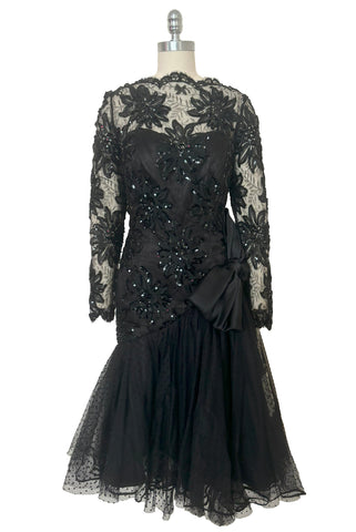 Front view of 1980s vintage black satin, sequin lace, & dotted tulle asymmetrical cocktail dress by Mignon, small to medium. New with tags. Showing the sweetheart strapless satin underlay and the lace & sequin straight neck, long sleeve overlay.