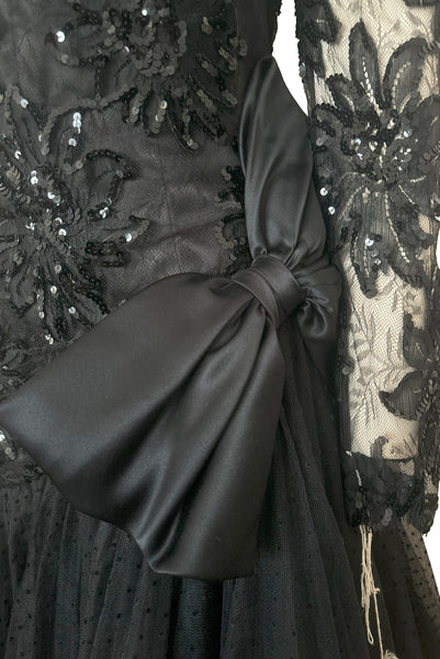 Front detail view of 1980s vintage black satin, sequin lace, & dotted tulle asymmetrical cocktail dress by Mignon, small to medium. New with tags. Showing the satin bow at the hip of the dropped asymmetrical waistline.