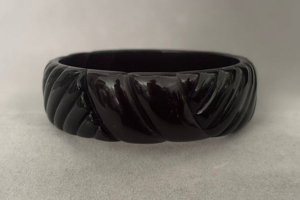 Horizontal front view of 1980s vintage black plastic molded bangle bracelet.