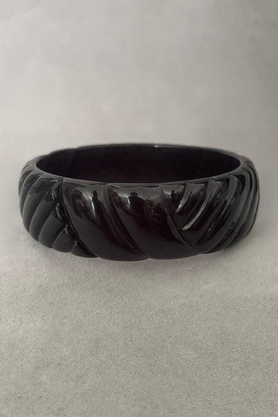 Vertical front view of 1980s vintage black plastic molded bangle bracelet.