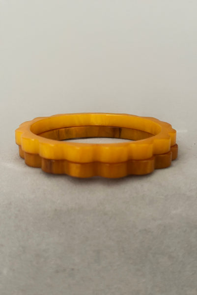 Vertical front view of 1930s vintage pair of yellow marbled egg yolk and butterscotch scalloped or daisy Bakelite bangle bracelet set of two (2).