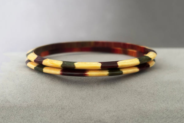 Horizontal front view of 1960s vintage cream, purple, and green celluloid two (2) bangle bracelet set. Showing the pair of bangles together.