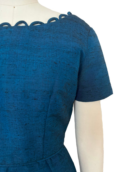 Detail view of 1950s vintage sapphire blue and black raw silk scalloped scoop neck, short sleeve, pencil skirt cocktail dress, size small to medium. Showing the piping at the waist and small shaping pleats at the waistline.