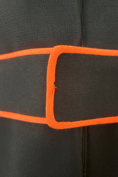 Belt detail view of 1970s vintage midi length black and orange wool coat with belt, by Gloria Sachs, size small to medium. Showing some moth damage and darkening to the orange trim on the belt end.