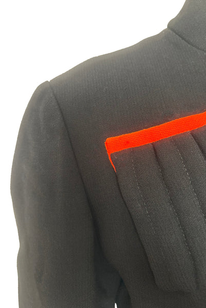 Detail view of 1970s vintage midi length black and orange wool coat with belt, by Gloria Sachs, size small to medium. Showing the padded chest pocket with orange trim.