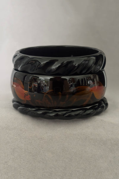 Vertical side view of 1980s vintage black plastic twisted, ridged, and orange goldfish painted bangle bracelet set of three (3).