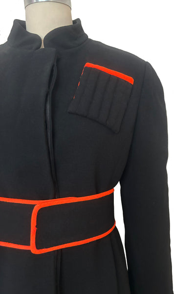 Detail view of 1970s vintage midi length black and orange wool coat with belt, by Gloria Sachs, size small to medium. Showing the padded chest pocket with orange trim and matching belt. 