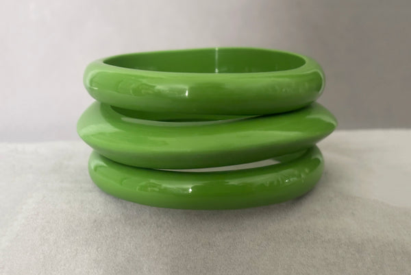Horizontal front view of 1980s vintage leaf green two (2) domed, and one (1) saucer three (3) bangle bracelet set. Showing the three bangles stacked.