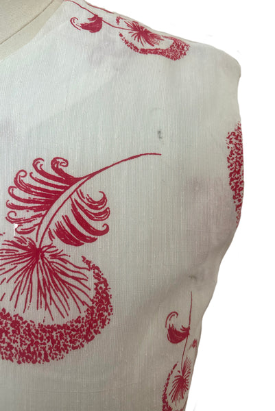 Detail view of 1960s vintage crew neck sleeveless white shantung sheath dress with red dandelion novelty floral print, size small to medium. Showing a dark spot in the slubbed fabric.