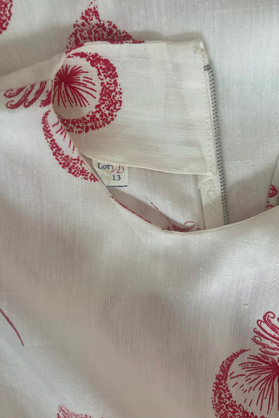 Interior detail view of 1960s vintage crew neck sleeveless white shantung sheath dress with red dandelion novelty floral print, size small to medium. Showing the size 13 tag.