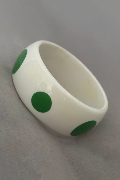 Vertical perspective view of 1980s vintage green and white polka dot plastic domed bangle bracelet.