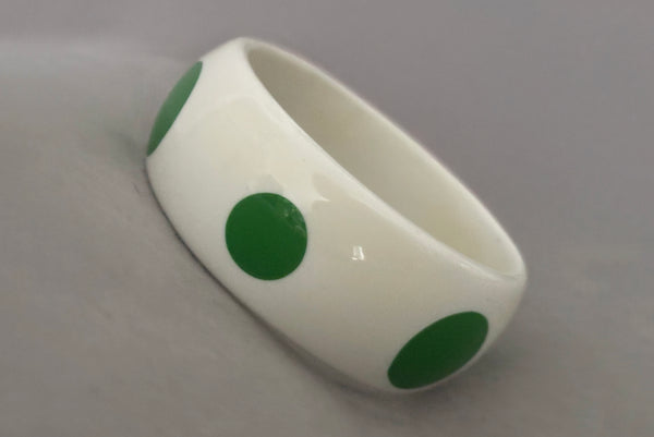 Horizontal perspective view of 1980s vintage green and white polka dot plastic domed bangle bracelet.