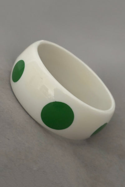 Vertical perspective view of 1980s vintage green and white polka dot plastic domed bangle bracelet.