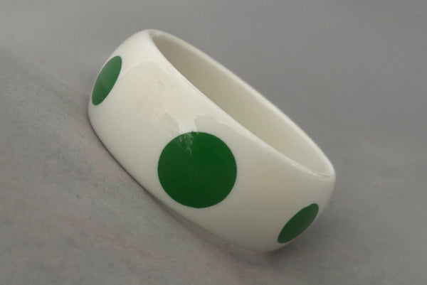 Horizontal perspective view of 1980s vintage green and white polka dot plastic domed bangle bracelet.