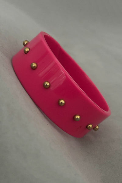 Vertical perspective view of 1980s vintage pink plastic oval bangle bracelet with gold tone metal studs.