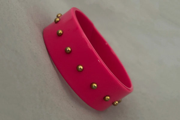 Horizontal perspective view of 1980s vintage pink plastic oval bangle bracelet with gold tone metal studs.
