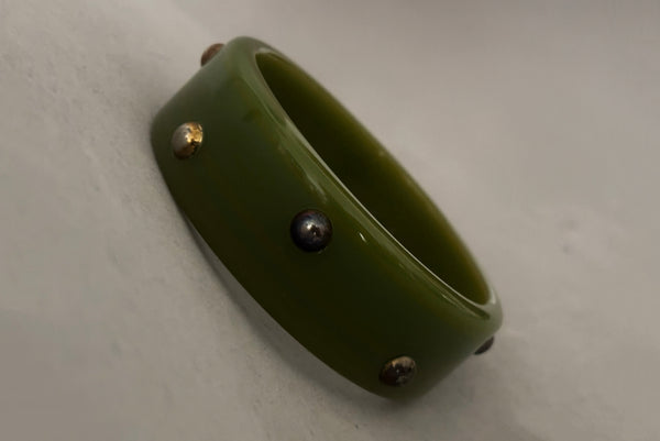 Horizontal perspective view of 1960s vintage striated green plastic bangle bracelet with gold tone studs. Showing discoloration of the studs.