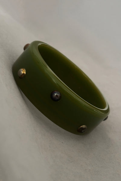 Vertical perspective view of 1960s vintage striated green plastic bangle bracelet with gold tone studs. Showing discoloration of the studs.