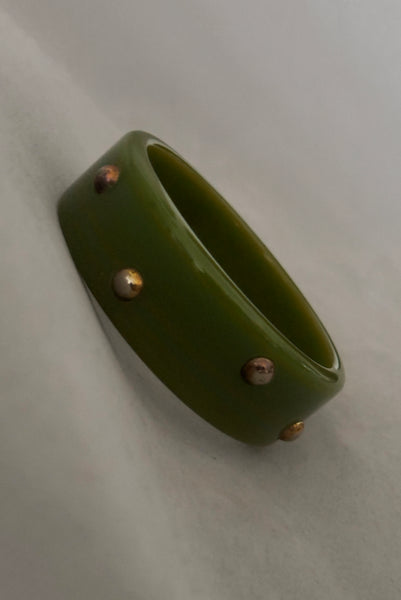 Vertical perspective view of 1960s vintage striated green plastic bangle bracelet with gold tone studs.