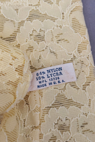 Interior detail view of 1960s vintage below elbow yellow stretch lace gloves. Showing the nylon/Lycra fabric content tag.