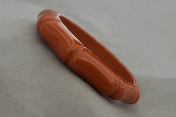 Horizontal perspective view of 2000s y2k vintage orange plastic molded faux bamboo bangle bracelet.
