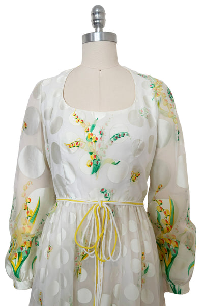 Bodice front view of 1960s vintage white chiffon, satin polka dot, yellow and green lily of the valley print floral maxi dress by Richilene New York for Neiman Marcus, size small to medium. Showing the scoop neckline, long full sleeves, and elevated waist with white and yellow cord bow belt.