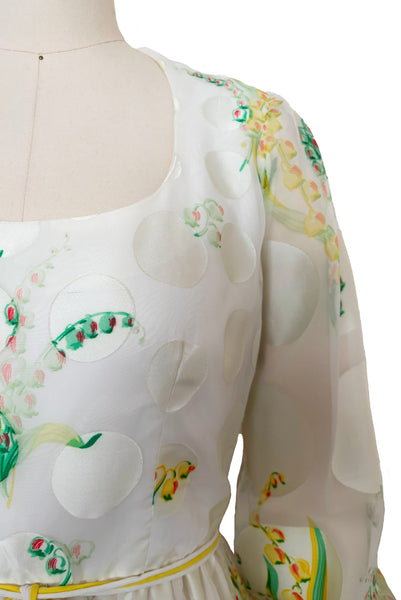 Detail view of 1960s vintage white chiffon, satin polka dot, yellow and green lily of the valley print floral maxi dress by Richilene New York for Neiman Marcus, size small to medium. Showing the scoop neckline, long full sleeves, and elevated waist with white and yellow cord bow belt.