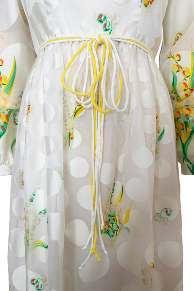 Detail view of 1960s vintage white chiffon, satin polka dot, yellow and green lily of the valley print floral maxi dress by Richilene New York for Neiman Marcus, size small to medium. Showing the long full sleeves, and elevated waist with white and yellow cord bow belt, and gathered skirt.