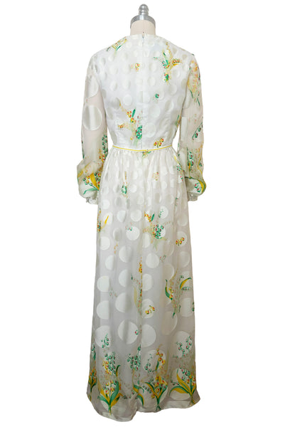 Back view of 1960s vintage white chiffon, satin polka dot, yellow and green lily of the valley print floral maxi dress by Richilene New York for Neiman Marcus, size small to medium. With scoop neck, long full sleeves, elevated waist, and floor length gathered skirt.