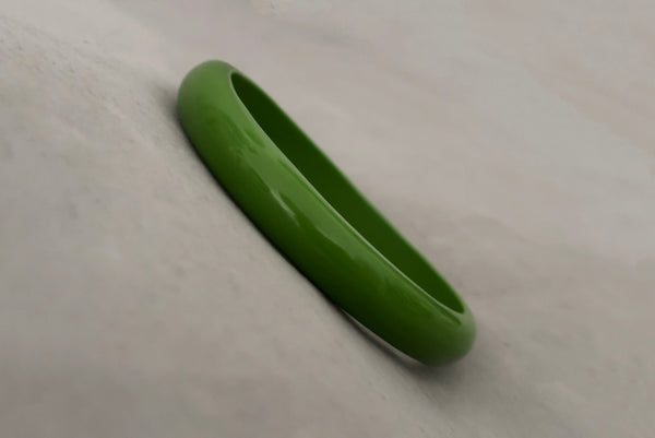 Horizontal perspective view of 1980s vintage leaf green two (2) domed, and one (1) saucer three (3) bangle bracelet set. Showing one domed bangle.