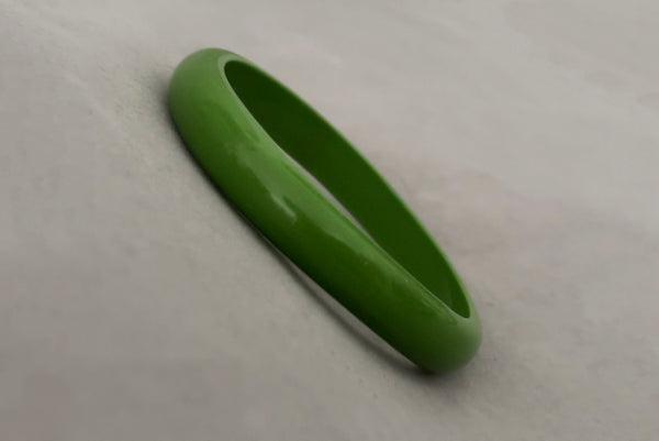 Horizontal perspective view of 1980s vintage leaf green two (2) domed, and one (1) saucer three (3) bangle bracelet set. Showing one domed bangle.