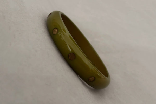 Horizontal perspective view of 1980s vintage green plastic two (2) bangle bracelet set inlaid with gold tone brass dots. Showing the lighter bangle.