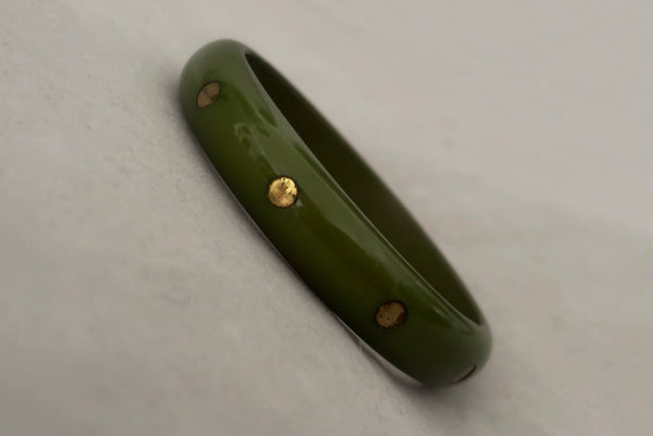 Horizontal perspective view of 1980s vintage green plastic two (2) bangle bracelet set inlaid with gold tone brass dots. Showing the darker bangle.