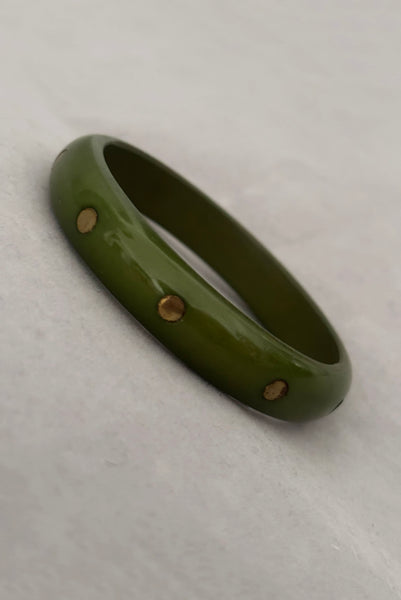 Vertical perspective view of 1980s vintage green plastic two (2) bangle bracelet set inlaid with gold tone brass dots. Showing the darker bangle.