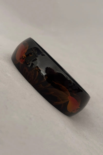 Vertical perspective view of 1980s vintage black plastic twisted, ridged, and orange goldfish painted bangle bracelet set of three (3). Showing the goldfish painted bangle only.