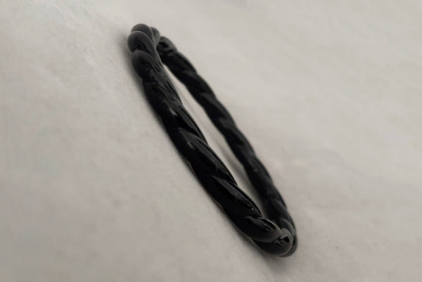 Horizontal perspective view of 1980s vintage black plastic twisted, ridged, and orange goldfish painted bangle bracelet set of three (3). Showing the twisted rope bangle only.