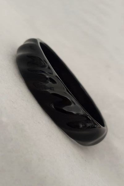 Vertical perspective view of 1980s vintage black plastic twisted, ridged, and orange goldfish painted bangle bracelet set of three (3). Showing the ridged bangle only.