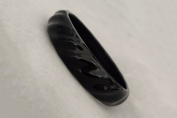 Horizontal perspective view of 1980s vintage black plastic twisted, ridged, and orange goldfish painted bangle bracelet set of three (3). Showing the ridged bangle only.