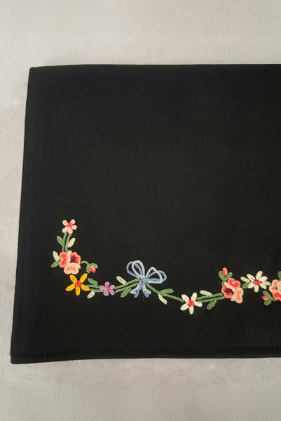 Detail view of 1930s vintage black satin clutch with pink, blue, green, purple, and gold floral chainstitch embroidered clutch by Denis Francet. Showing  a close-up of the flower and bow embroidery.