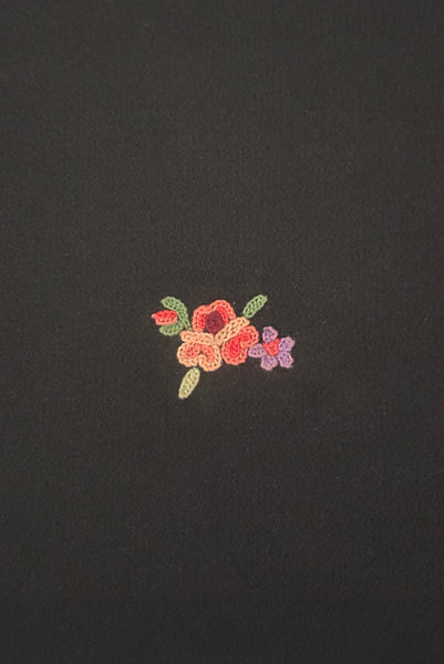 Detail view of 1930s vintage black satin clutch with pink, blue, green, purple, and gold floral chainstitch embroidered clutch by Denis Francet. Showing  a close-up of the flower and bow embroidery.