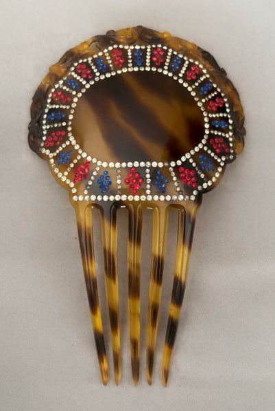 Vertical front view of 1920s vintage early plastic marbled brown tortoise hair comb with clear, red, and blue rhinestones.