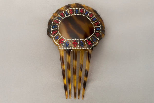 Horizontal front view of 1920s vintage early plastic marbled brown tortoise hair comb with clear, red, and blue rhinestones.