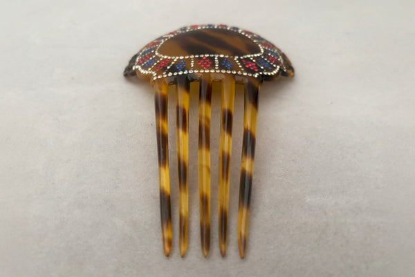 Horizontal perspective view of 1920s vintage early plastic marbled brown tortoise hair comb with clear, red, and blue rhinestones.