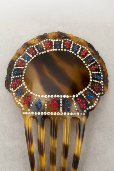 Detail view of 1920s vintage early plastic marbled brown tortoise hair comb with clear, red, and blue rhinestones. Showing that some of the clear rhinestone shave darkened.