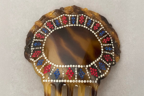 Detail view of 1920s vintage early plastic marbled brown tortoise hair comb with clear, red, and blue rhinestones. Showing that some of the clear rhinestone shave darkened.