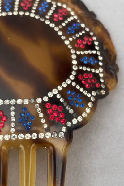 Detail view of 1920s vintage early plastic marbled brown tortoise hair comb with clear, red, and blue rhinestones. Showing that some of the clear rhinestone shave darkened.