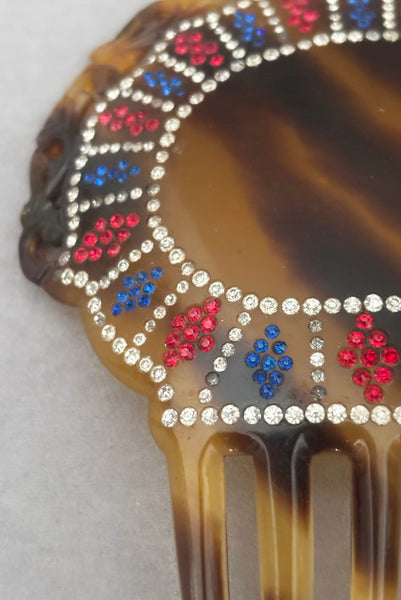 Detail view of 1920s vintage early plastic marbled brown tortoise hair comb with clear, red, and blue rhinestones. Showing that some of the clear rhinestone shave darkened.